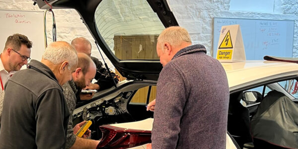 A trainer (Pete Banks) overseeing some learners working at the back of a plug in hybrid vehicle.