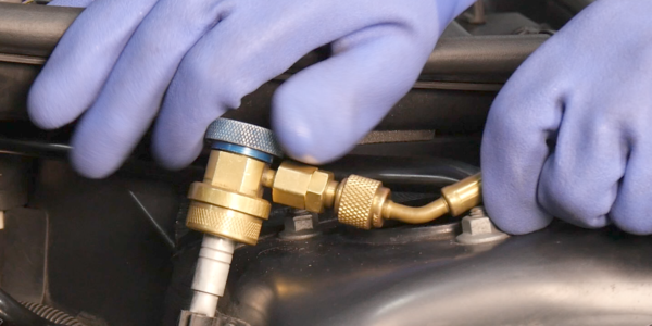 An automotive air conditioning low pressure union being tightened by someone wearing refrigerant resistive gloves.